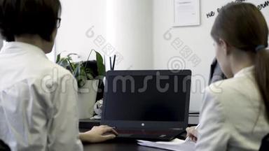 在办公室工作的两个女孩的后视图，看看带有空白可编辑绿色屏幕的笔记本电脑。 商业妇女的概念